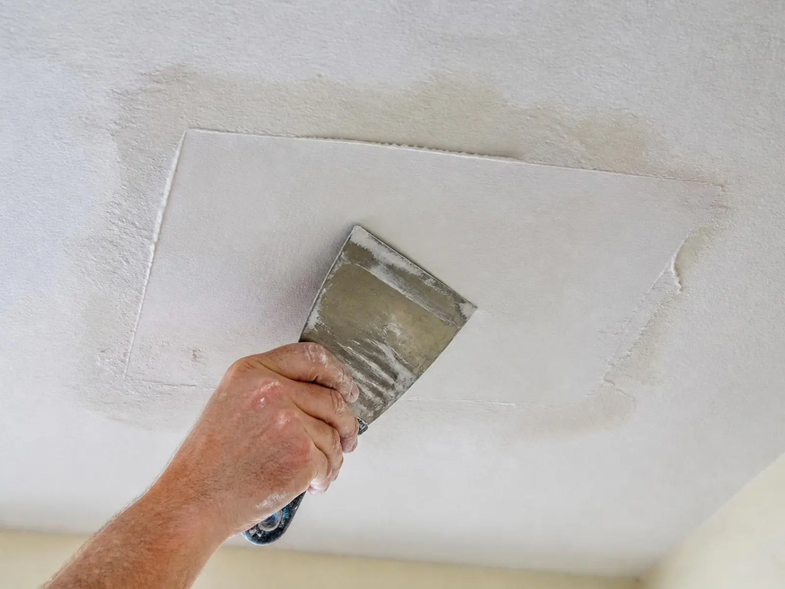 Hand smoothing joint compound over a square drywall patch on a ceiling